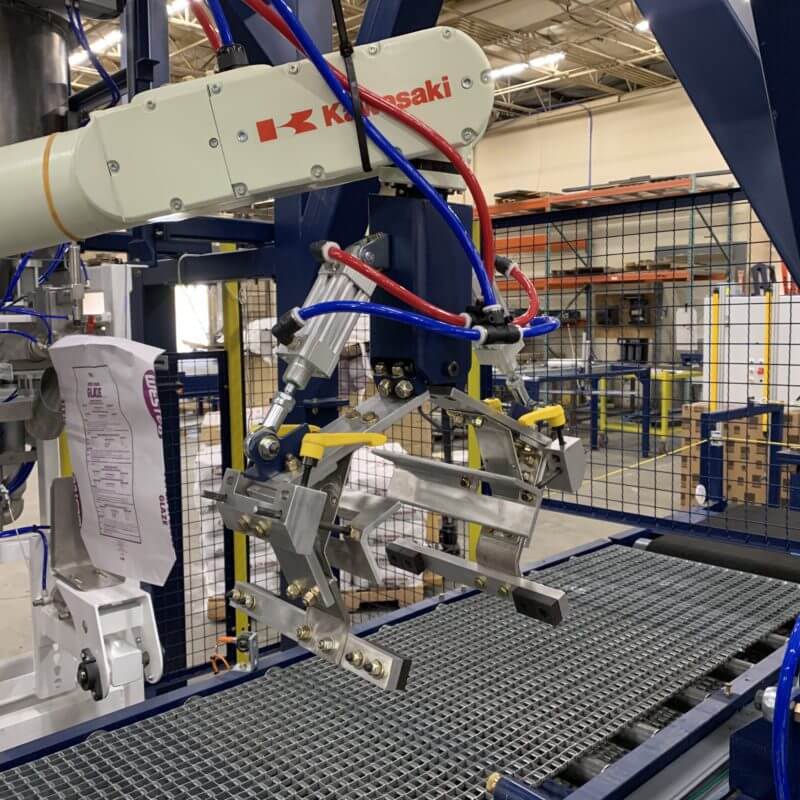 A Kawasaki industrial robot arm is positioned above a conveyor belt, likely engaged in a manufacturing process within a factory setting.
