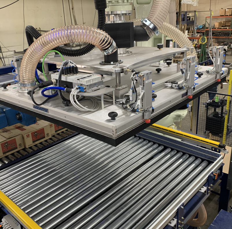 An industrial robotic arm equipped with suction grippers is positioned over a conveyor system, likely ready to manipulate objects within a factory setting.