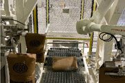 A robotic arm is handling cardboard boxes on a conveyor belt within an industrial setting.