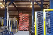 A blurry industrial warehouse scene with a pallet of red bags stacked and mechanical equipment nearby.