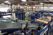 Machinery with conveyor belts is processing materials in a busy industrial facility with an array of blue and yellow equipment.